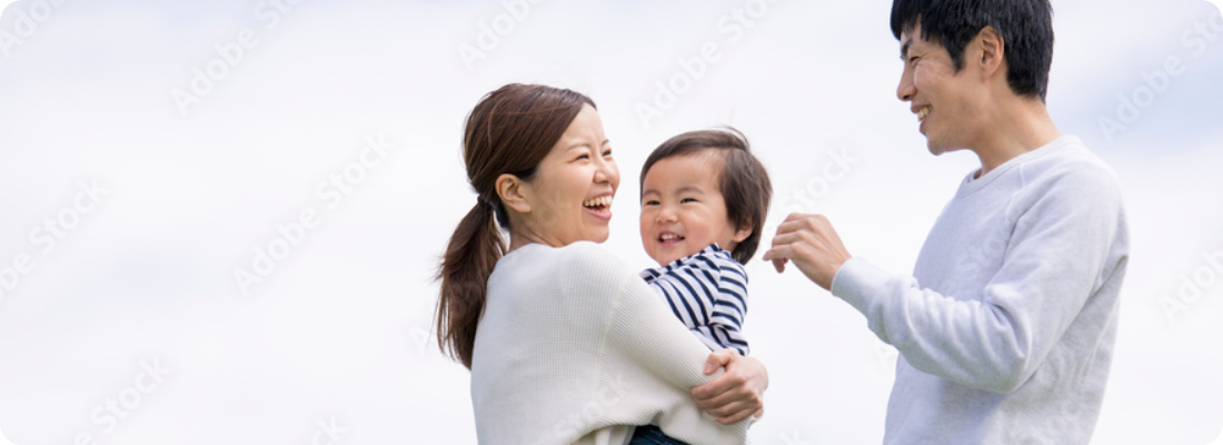 屋外で父母に抱きかかえられ笑顔で過ごす幼い子どもと家族の写真