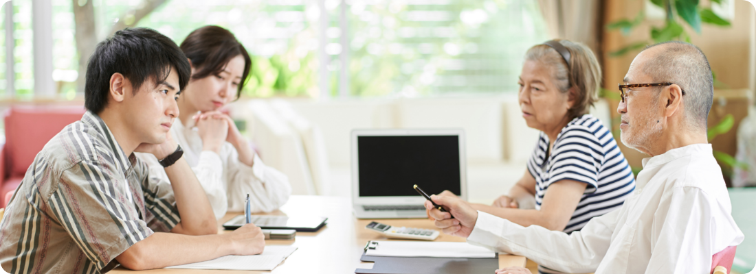 シニア夫婦と若い夫婦がテーブルで話し合っている様子