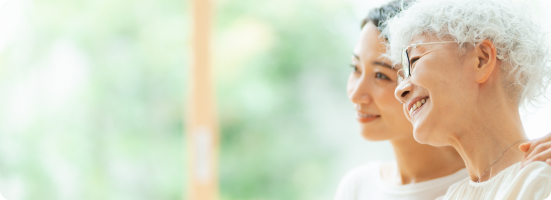 高齢女性の肩を抱き寄り添う女性の笑顔の写真