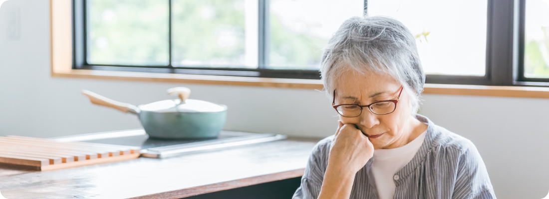 室内で一人悩んだ様子で考え込む高齢女性の写真